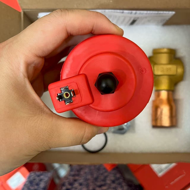 Red coil held by hand, showing the top terminal structure.