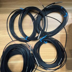 Multiple coiled temperature sensors with stainless steel probes and black cables, neatly arranged on a wooden surface.