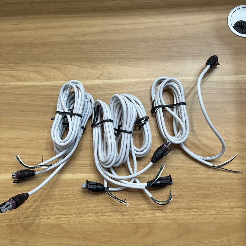 Multiple white cables with waterproof connectors, bundled on a wooden table.