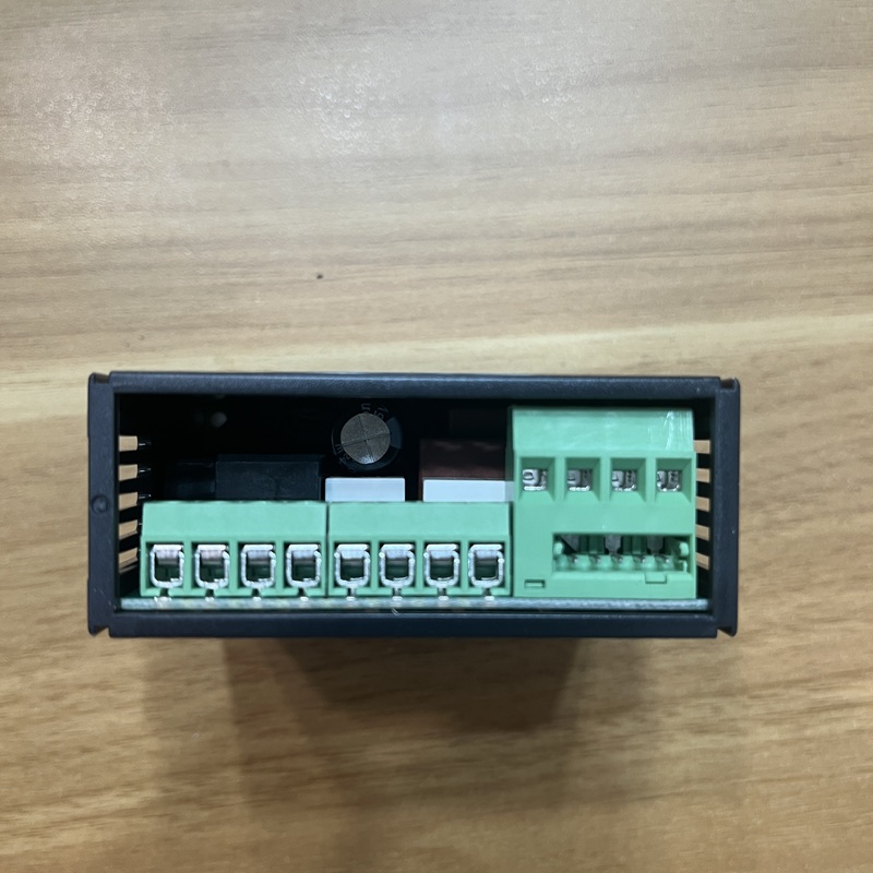 Close-up of wiring terminals at the bottom of temperature controller, two groups of green pluggable terminals, internal circuit board components visible